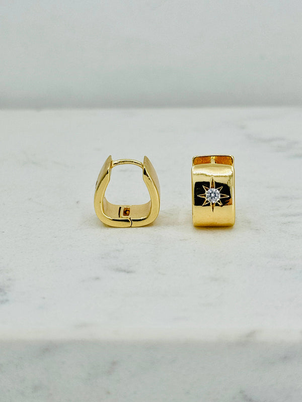 a pair of yellow gold earrings sitting on top of a white counter