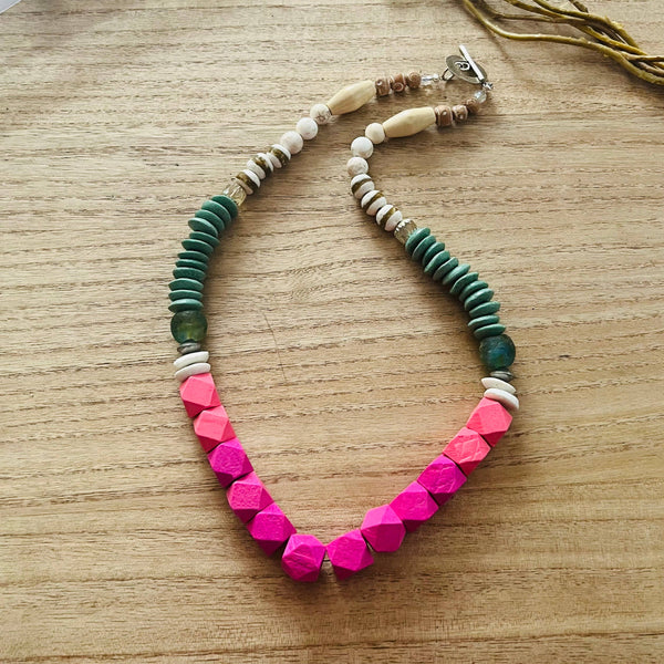 a pink and green necklace on a wooden table