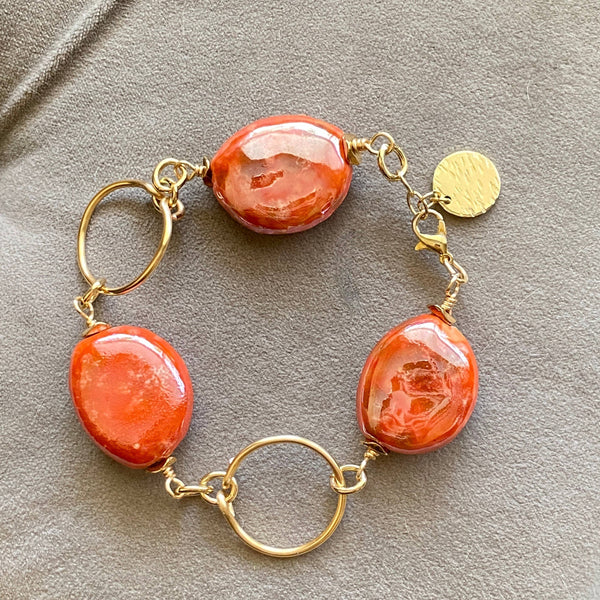 a bracelet with two orange beads and a gold disc