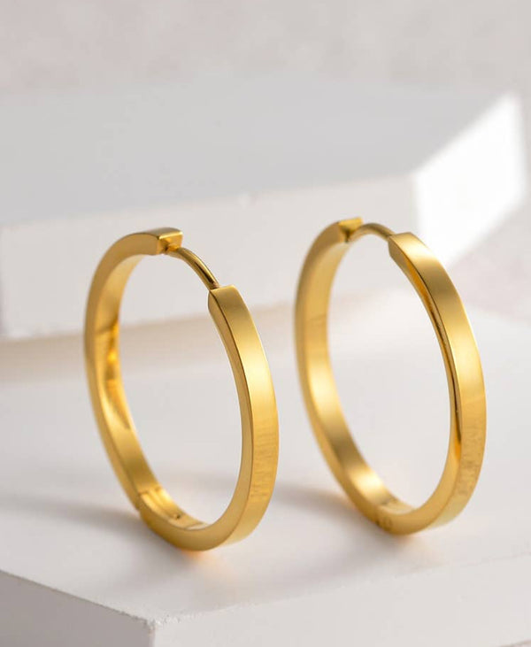 a pair of gold hoop earrings on a white surface